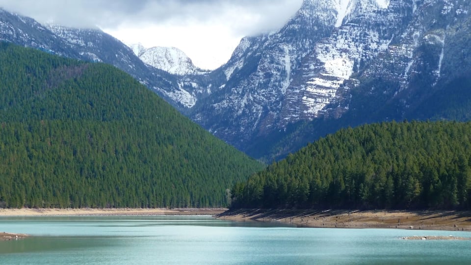 A lake surrounded by forested mountains with snow-capped peaks.