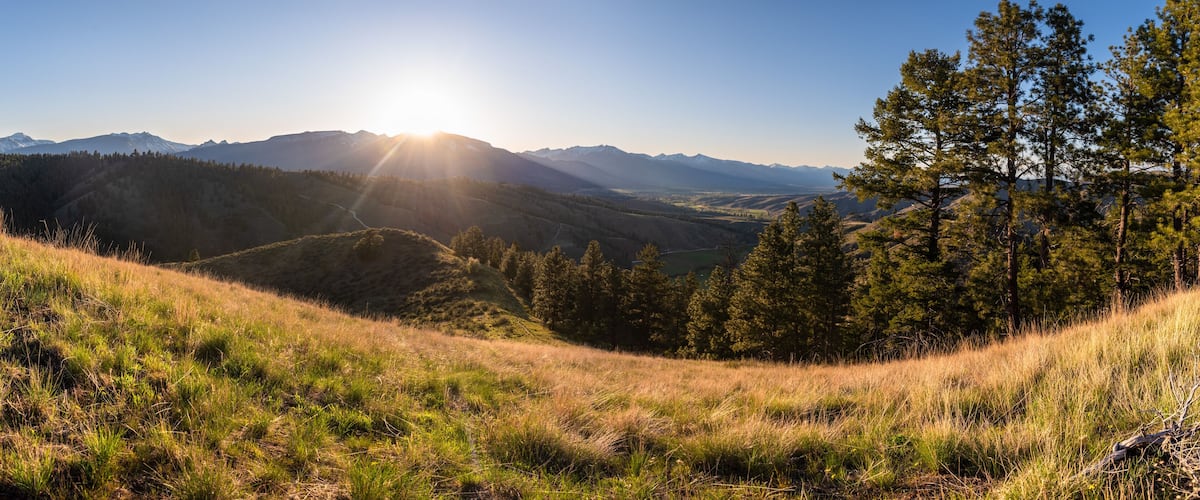 A mountainous landscape with a clear sky, a sunlit valley, and dense forests.
