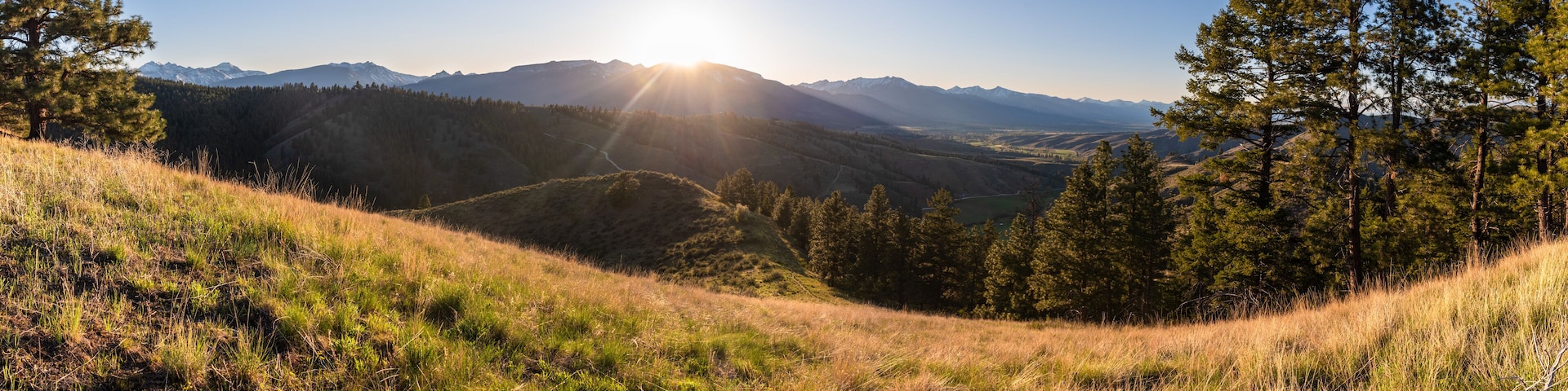 A mountainous landscape with a clear sky, a sunlit valley, and dense forests.