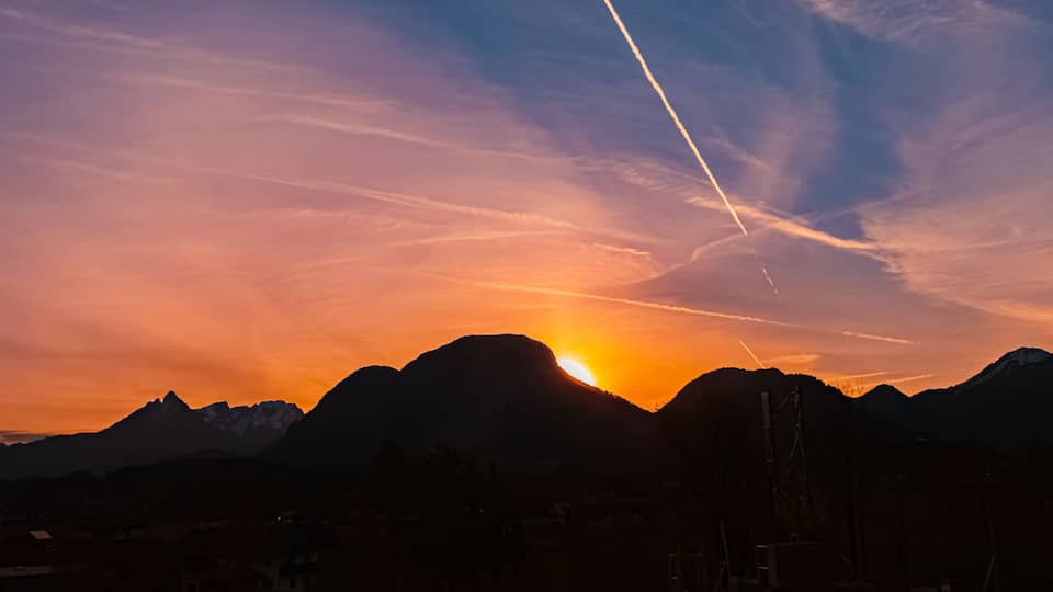A sunset over a mountain range with a visible contrail.