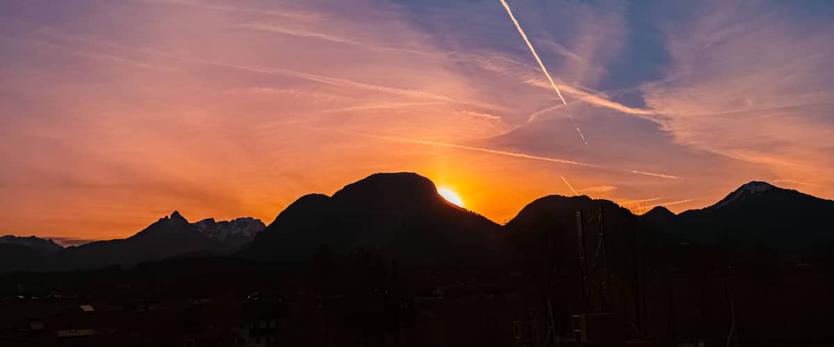 A sunset over a mountain range with a visible contrail.