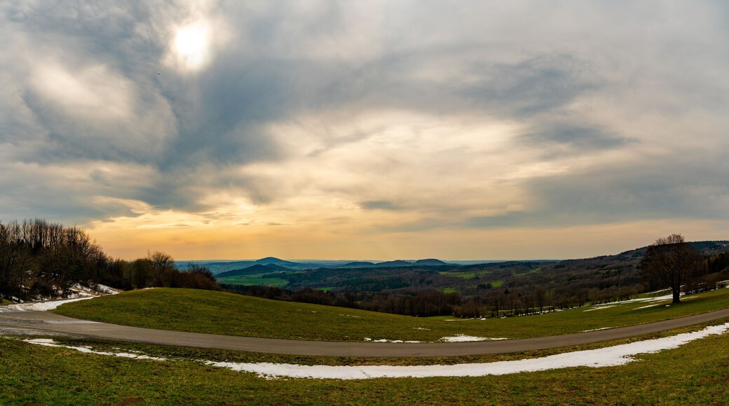 A landscape with a winding road, snow patches, and a cloudy sky.