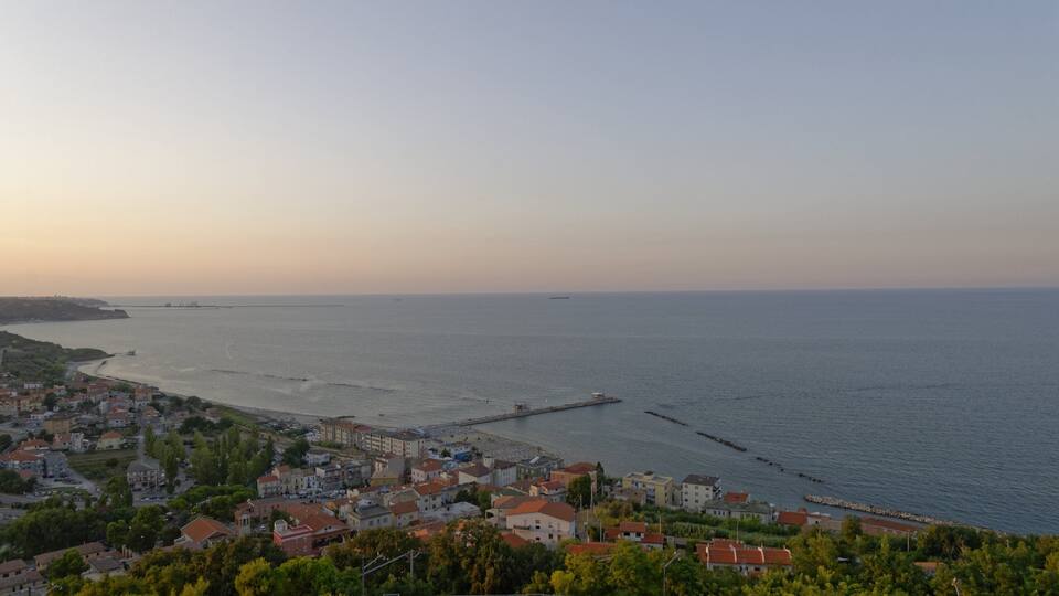 A coastal town with a pier extending into the sea, surrounded by buildings and greenery.