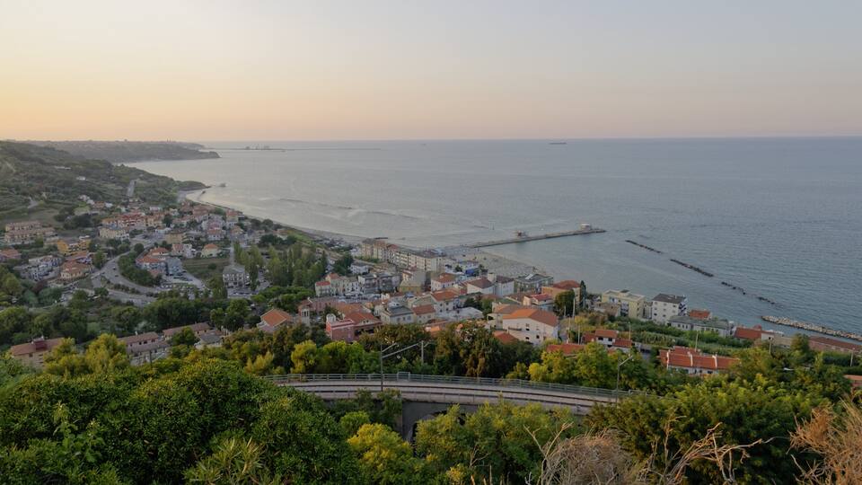 A coastal town with a bridge, buildings, and a pier extending into the sea.