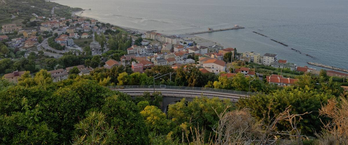 A coastal town with a bridge, buildings, and a pier extending into the sea.