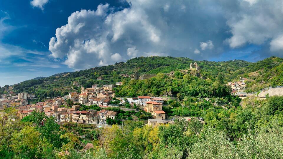 A hillside town with buildings nestled among lush greenery and a prominent ancient ruin.