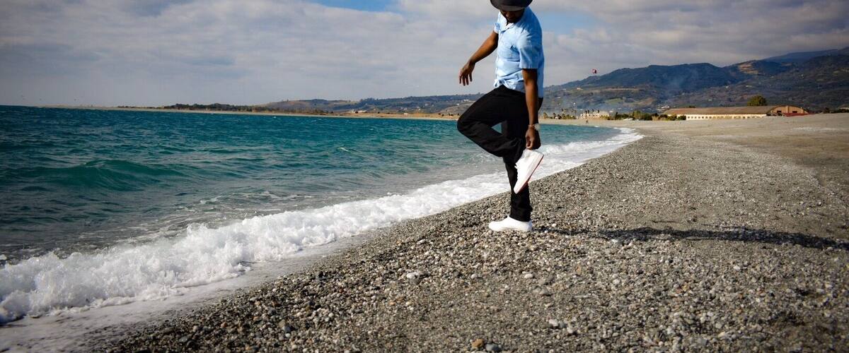 A person standing on a pebble beach with the ocean in the background.