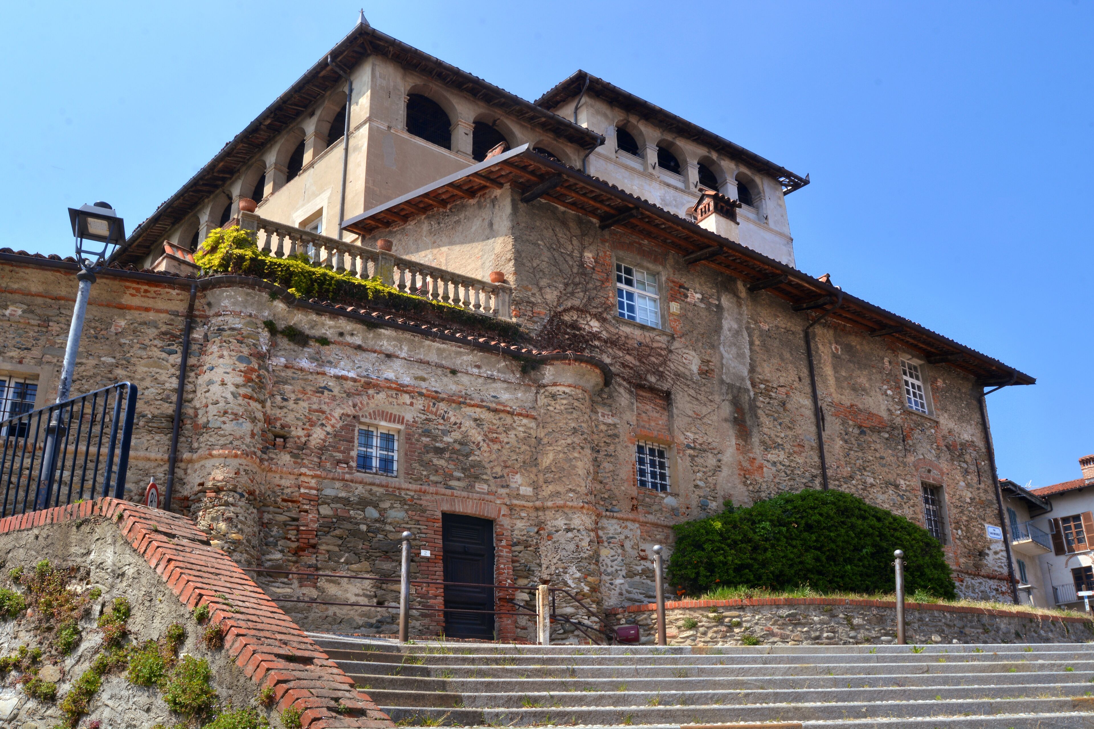A historic stone building with a red-tiled roof, a balcony, and a bell tower.