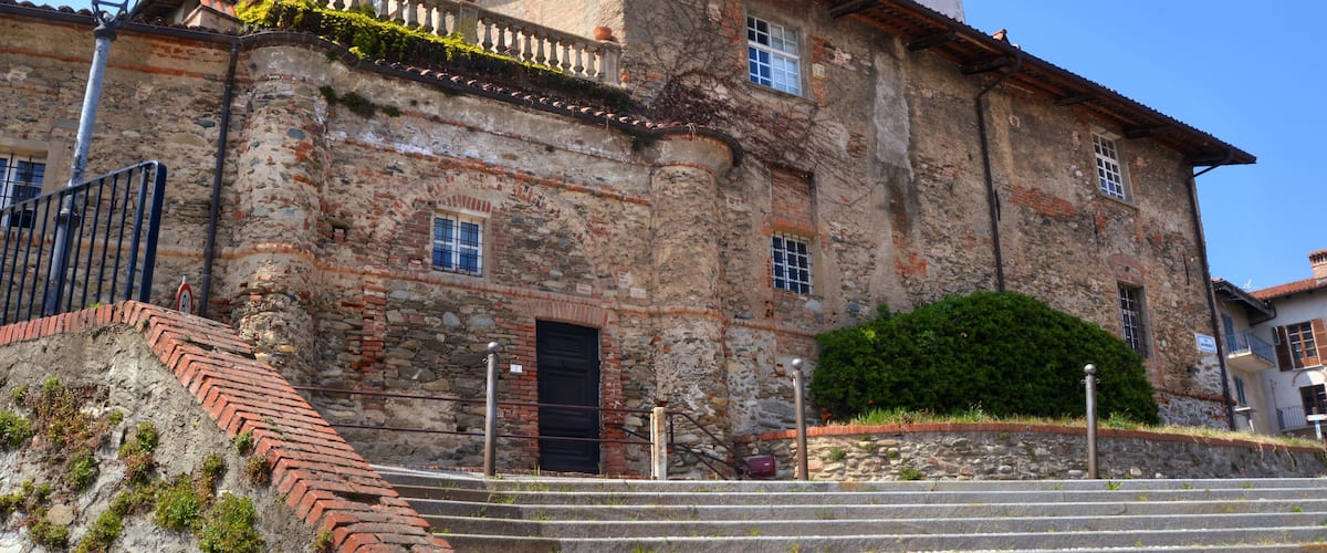A historic stone building with a red-tiled roof, a balcony, and a bell tower.