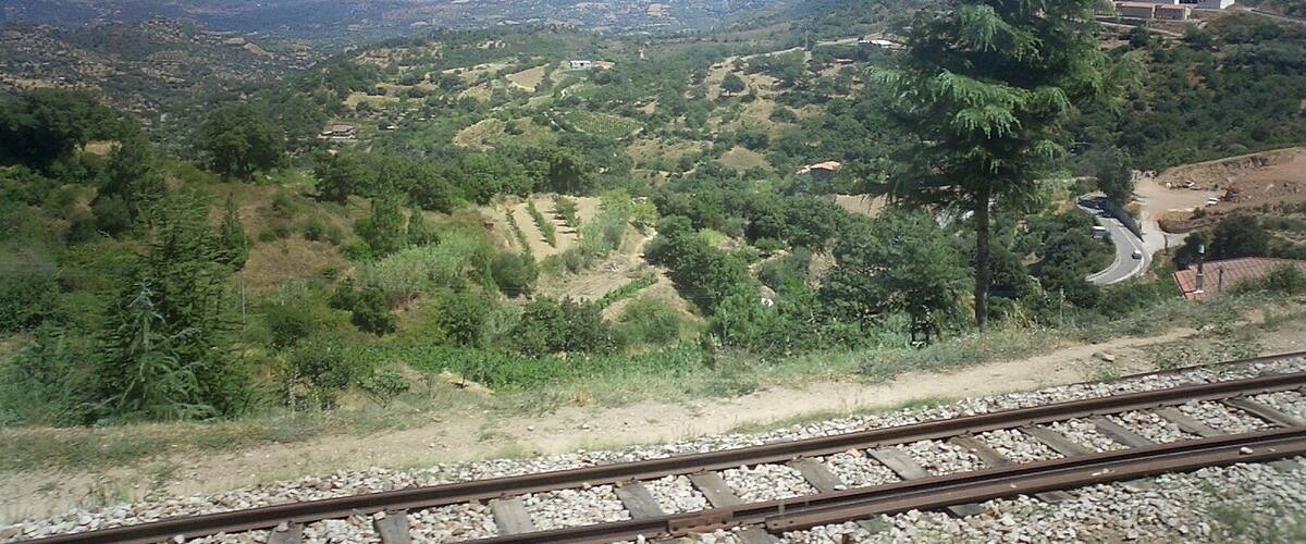 A mountainous landscape with a railway track, dense greenery, and distant hills.