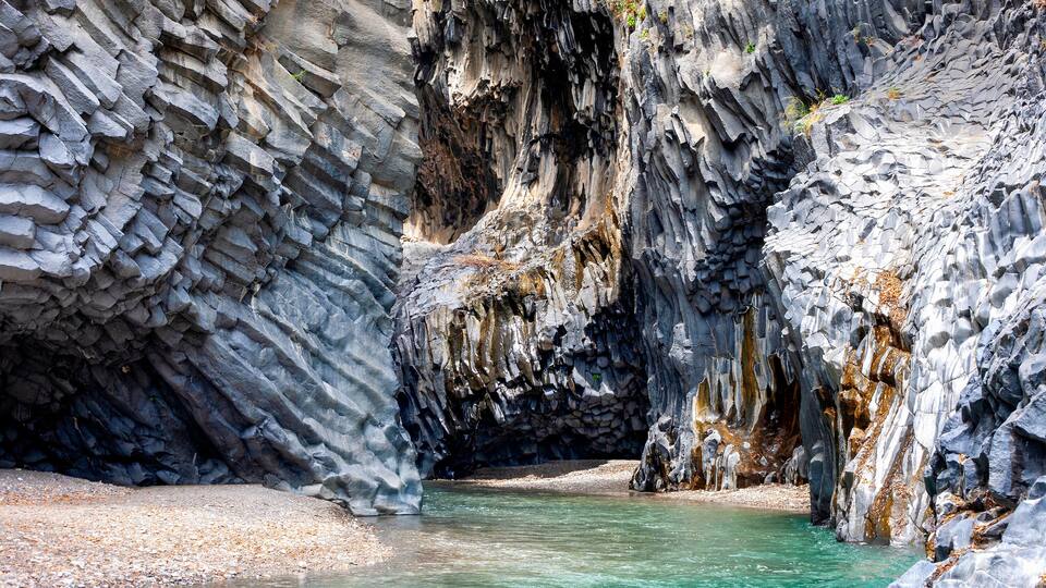 A rocky canyon with clear turquoise water and a pebbly shore.