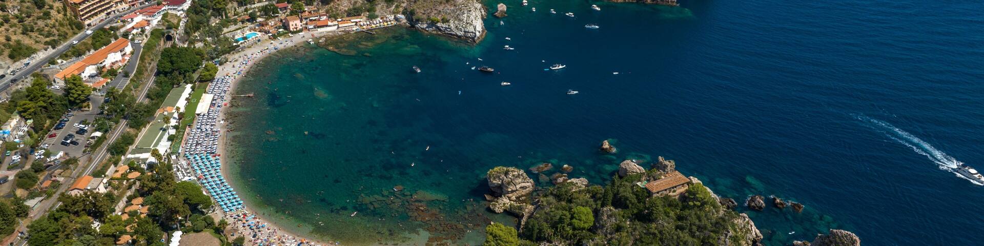 An aerial view of a coastal town with a beach, rocky outcrops, and clear blue waters.