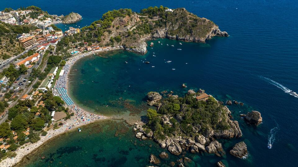 An aerial view of a coastal town with a beach, rocky outcrops, and clear blue waters.