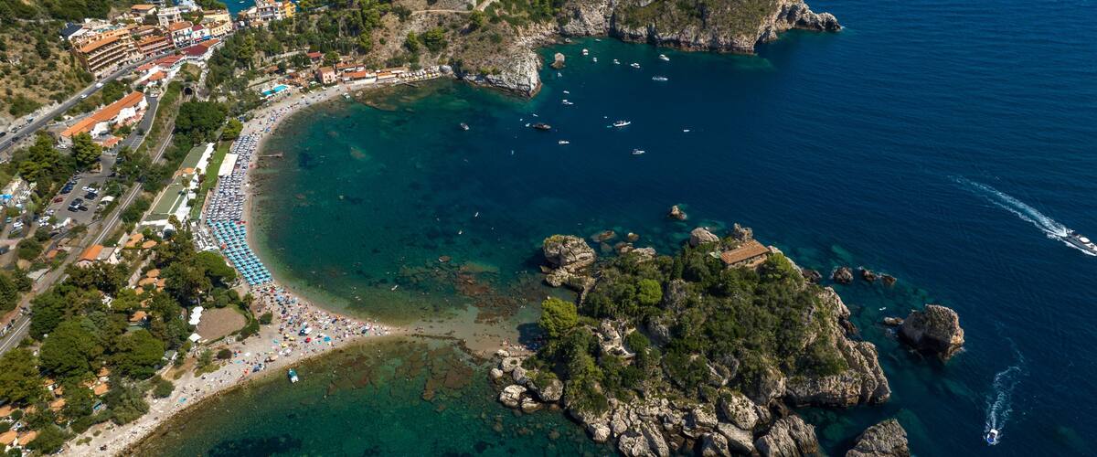 An aerial view of a coastal town with a beach, rocky outcrops, and clear blue waters.