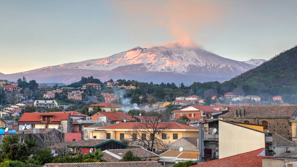 A town with red-tiled roofs and a snow-capped mountain in the background.