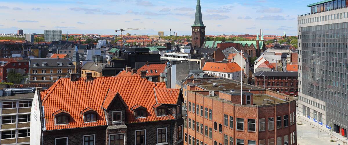 A cityscape with a prominent church steeple, red-roofed buildings, and modern high-rises.