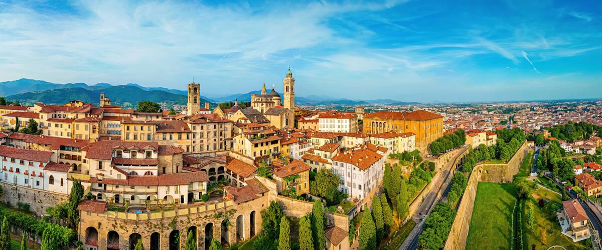 A panoramic view of a historic town with prominent architecture, a river, and surrounding mountains.