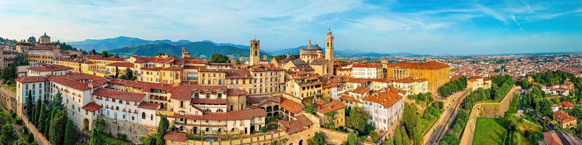 A panoramic view of a historic town with prominent architecture, a river, and surrounding mountains.