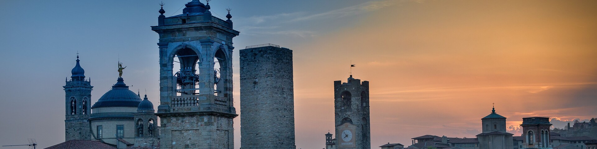 Un paisaje urbano histórico con torres destacadas y edificios con cúpulas bajo un cielo al atardecer.
