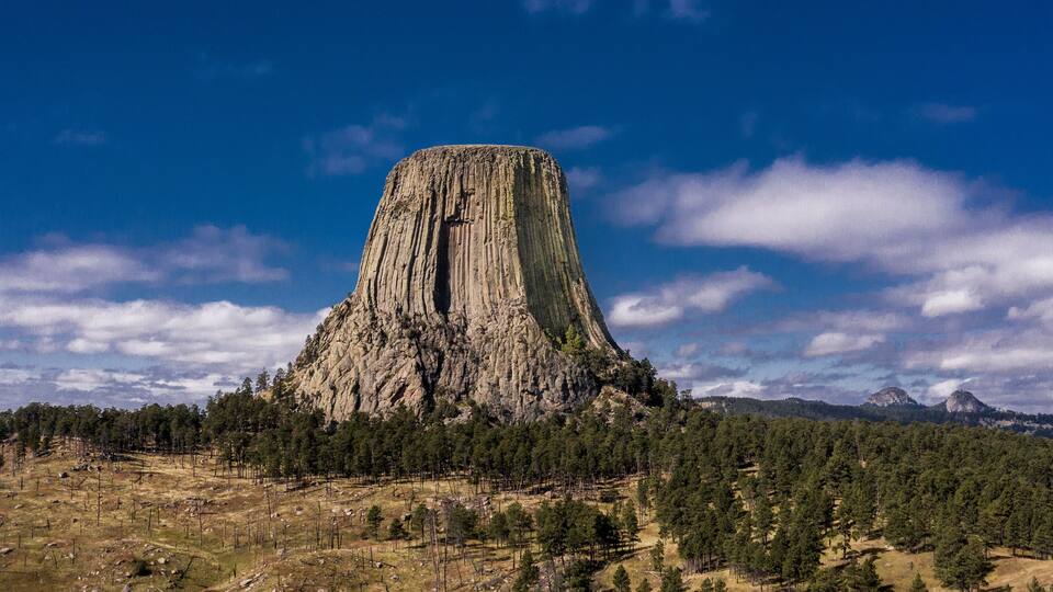 A large, steep-sided rock formation surrounded by dense forest.