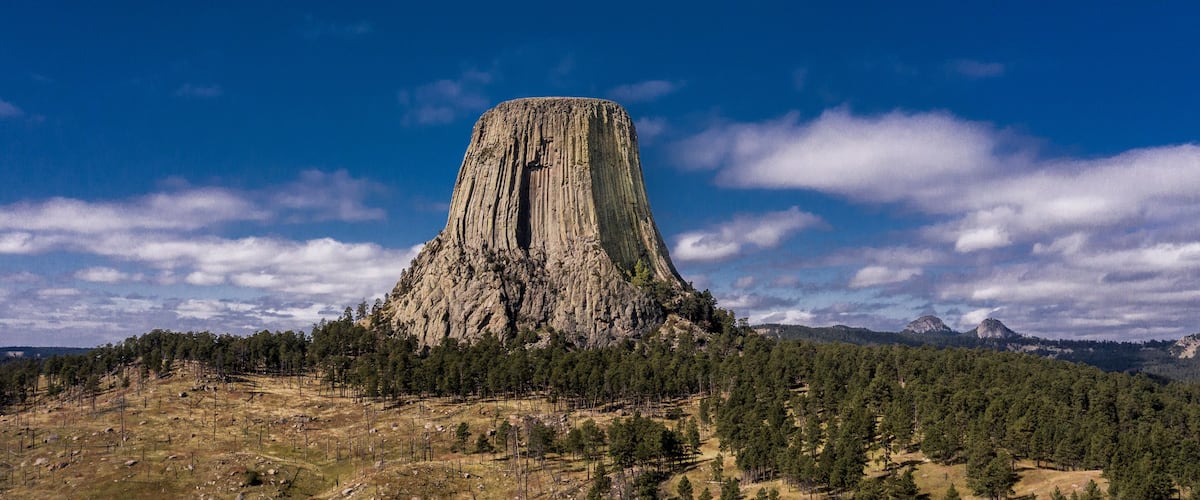A large, steep-sided rock formation surrounded by dense forest.