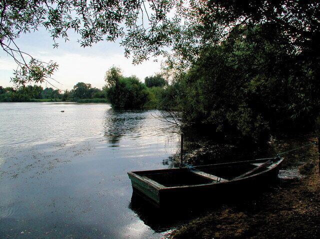 A calm river with a small boat docked on the shore, surrounded by trees.