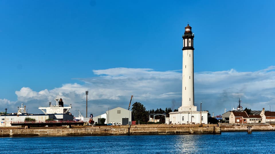 A lighthouse, a dock with a ship, and a small town by the water.
