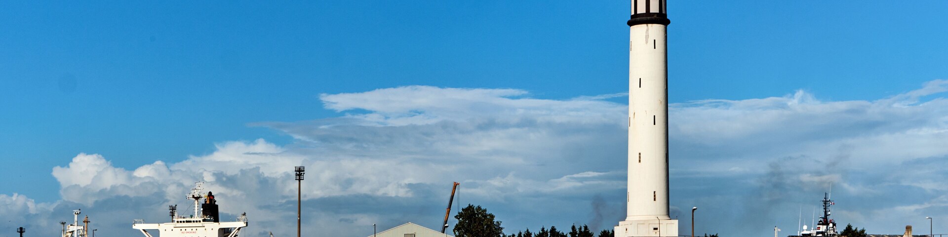 Un faro, un muelle con un barco y un pequeño pueblo junto al agua.