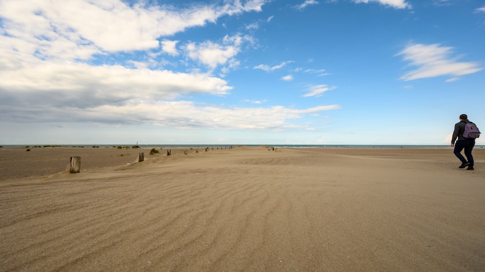 A vast sandy beach with a clear sky and scattered clouds.