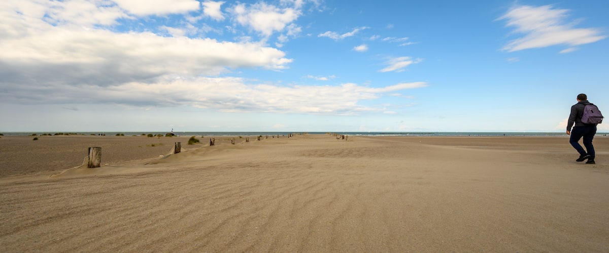 A vast sandy beach with a clear sky and scattered clouds.