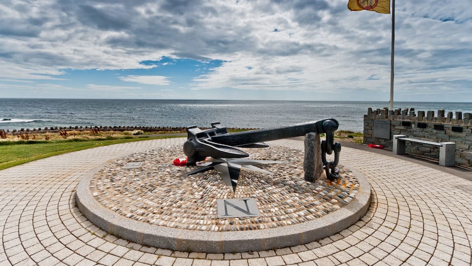 A cannon on a circular stone platform with a flag, overlooking the ocean.