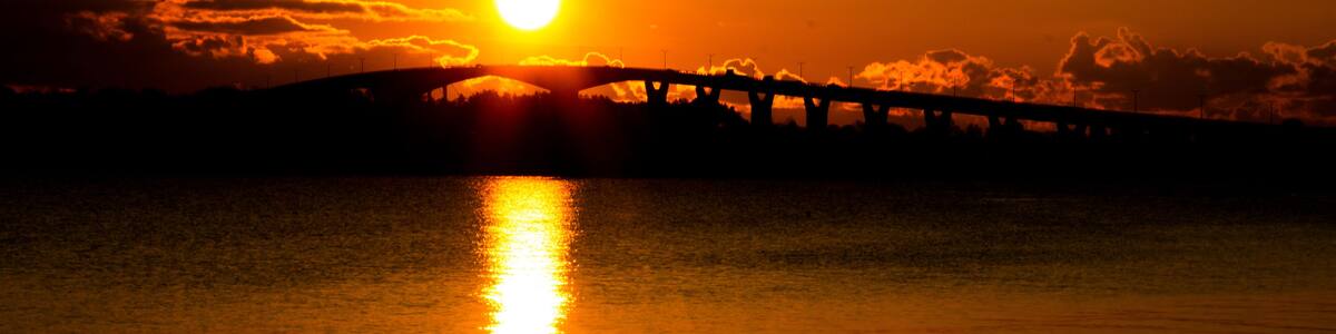 A sunset over a calm body of water with a bridge silhouetted against the sky.