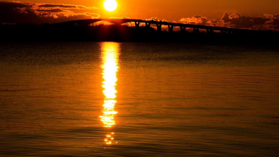 A sunset over a calm body of water with a bridge silhouetted against the sky.