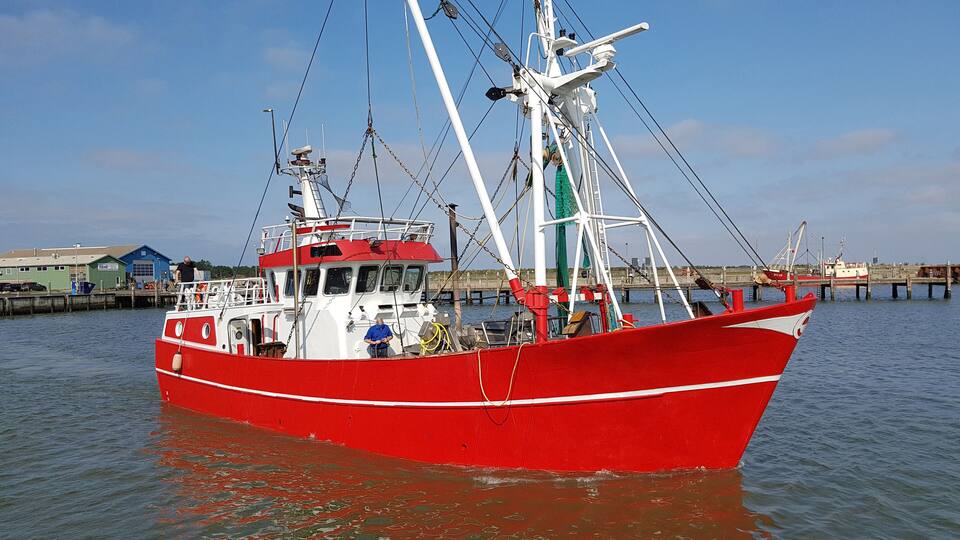 A red fishing boat docked at a pier with a clear sky in the background.