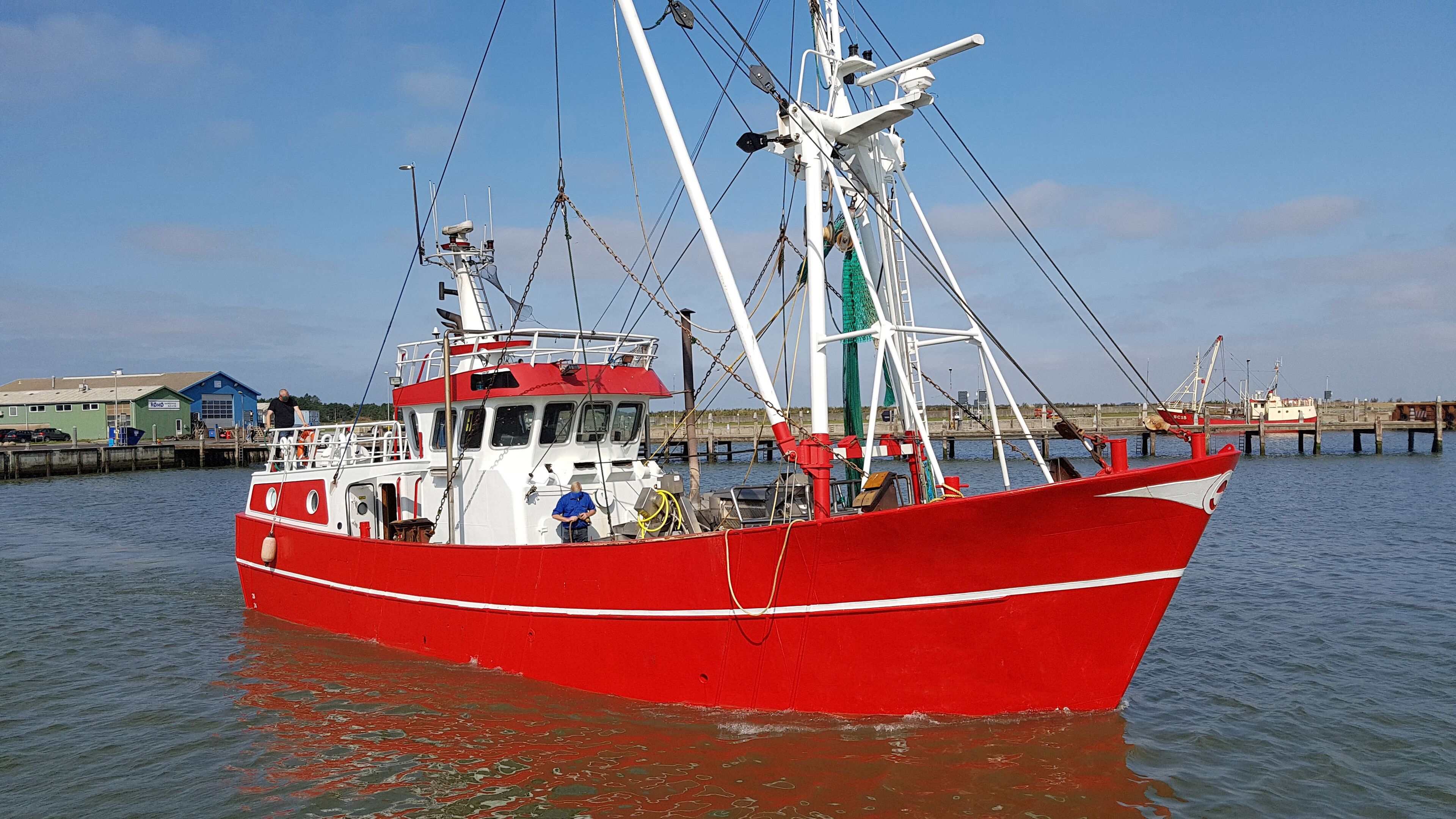 A red fishing boat docked at a pier with a clear sky in the background.
