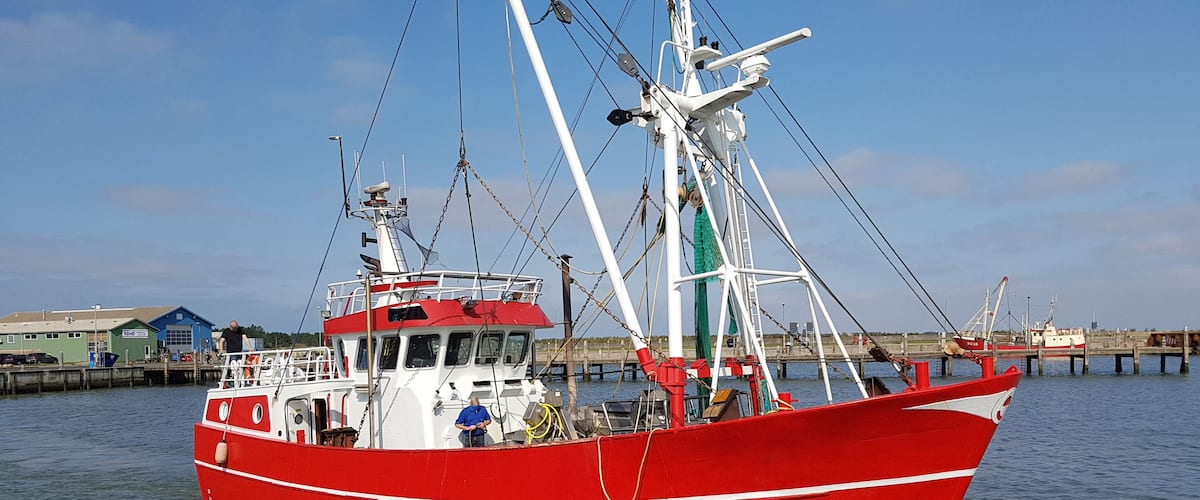 A red fishing boat docked at a pier with a clear sky in the background.