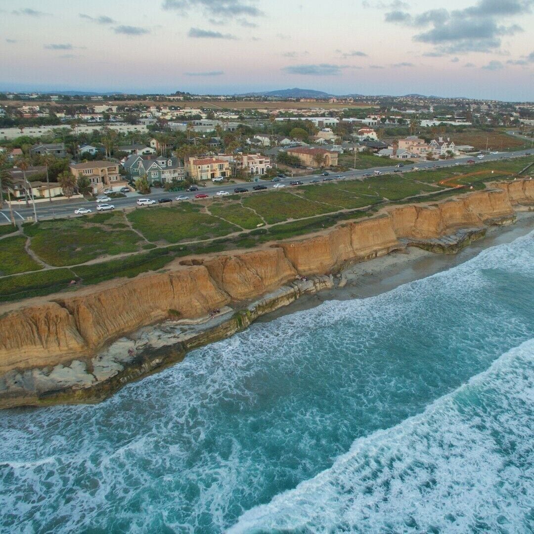 Un pueblo costero con un acantilado destacado, una playa y edificios residenciales.