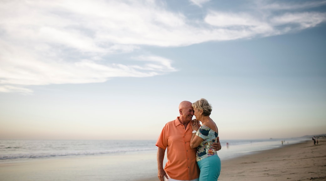 Romantic senior couple looking at each other while standing by sea against sky during sunset