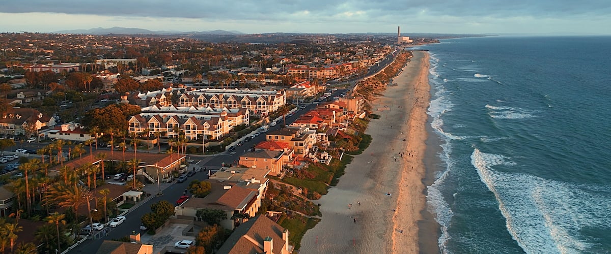 A coastal cityscape with a beach, residential buildings, and a distant industrial structure.