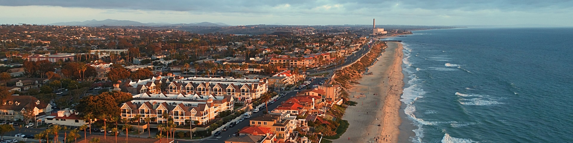 A coastal cityscape with a beach, residential buildings, and a distant industrial structure.