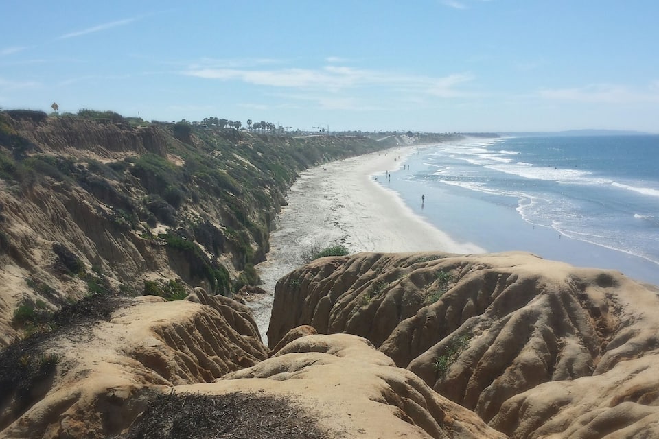 Un paisaje costero con una playa arenosa, acantilados y el océano.