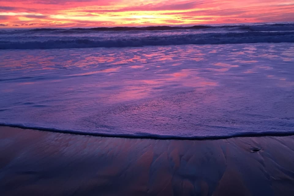 A beach at sunset with waves and a pink sky.