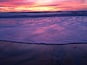 A beach at sunset with waves and a pink sky.