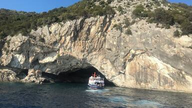A boat navigating through a rocky coastal area with a cave entrance.