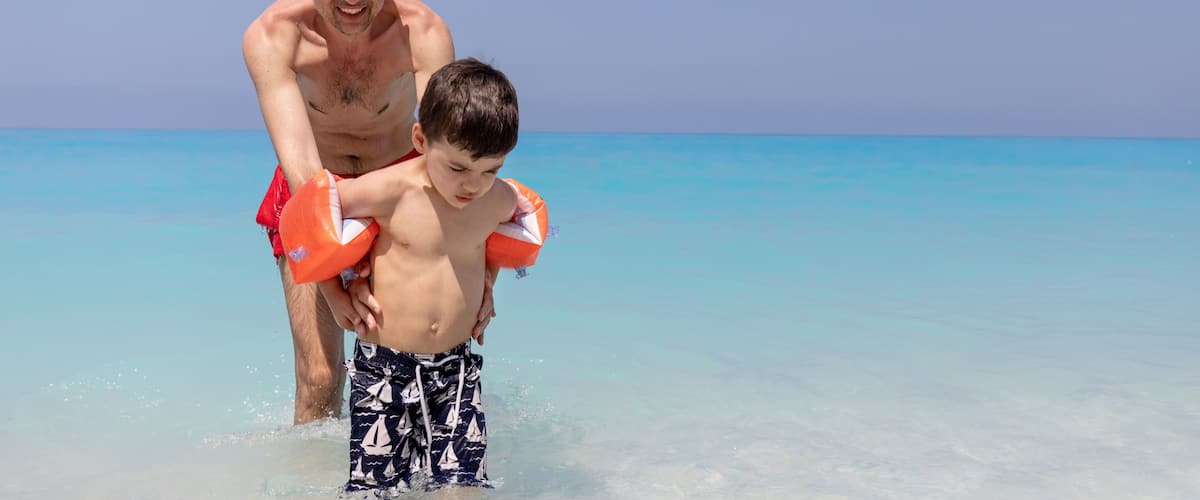 A beach with clear turquoise water and a person carrying another on their shoulders.