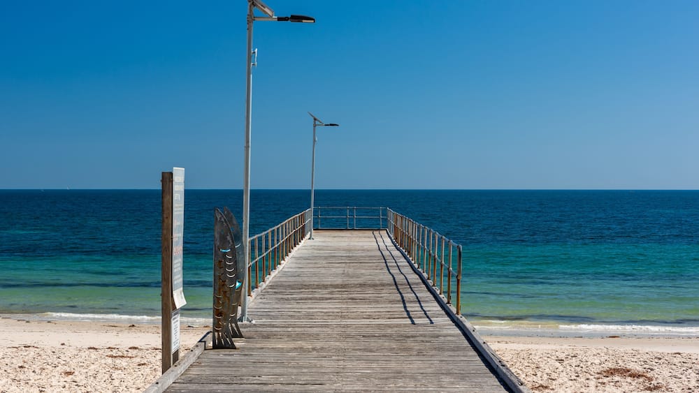 A wooden pier extending into a calm sea with clear skies.