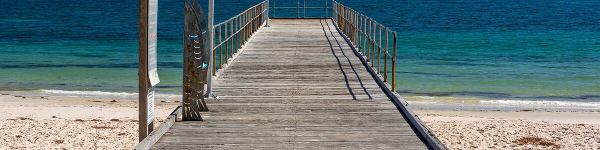 A wooden pier extending into a calm sea with clear skies.