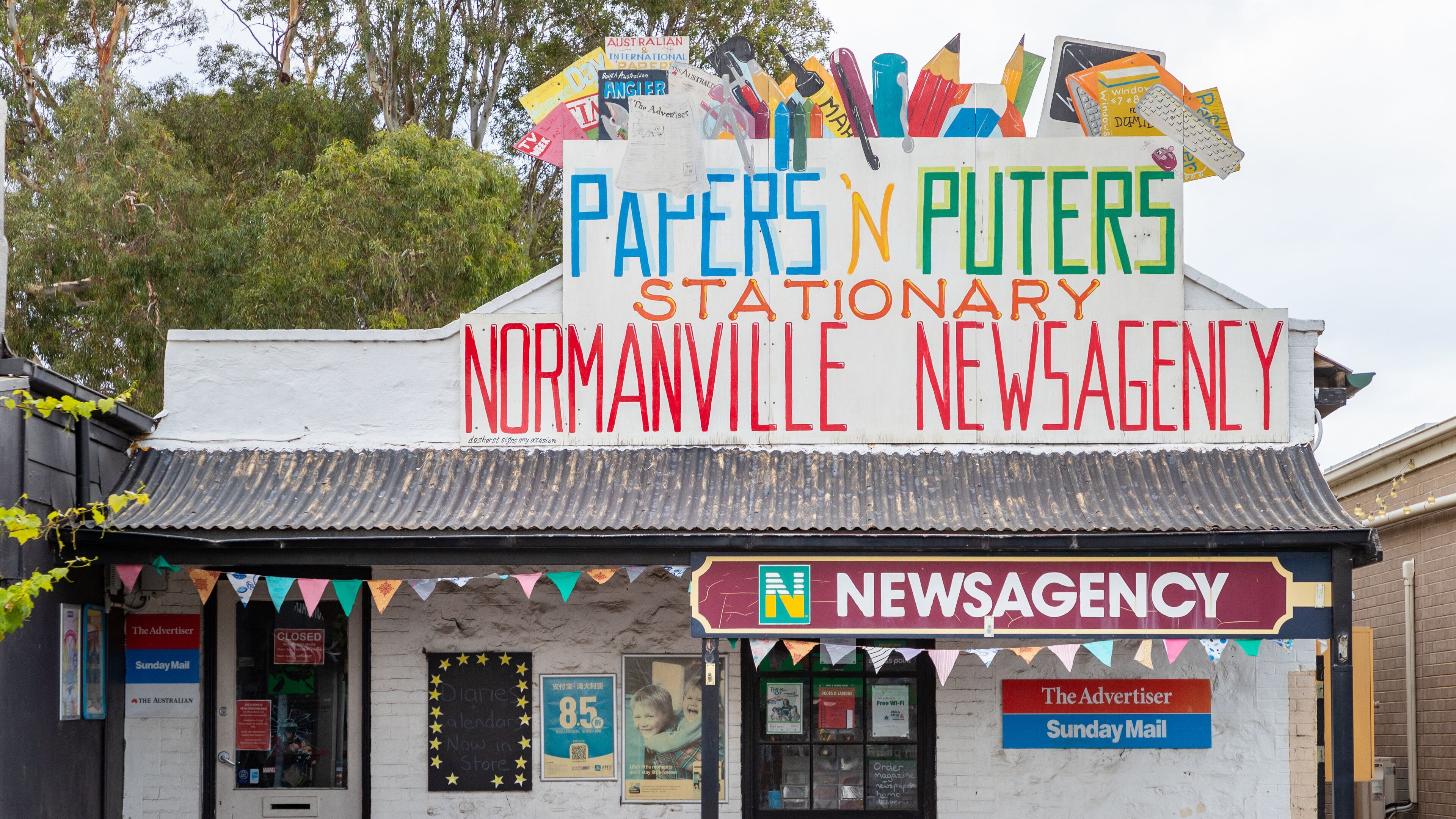 A stationary news agency with a colorful signboard and various advertisements.