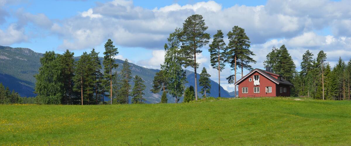 A red cabin in a grassy field with mountains in the background.