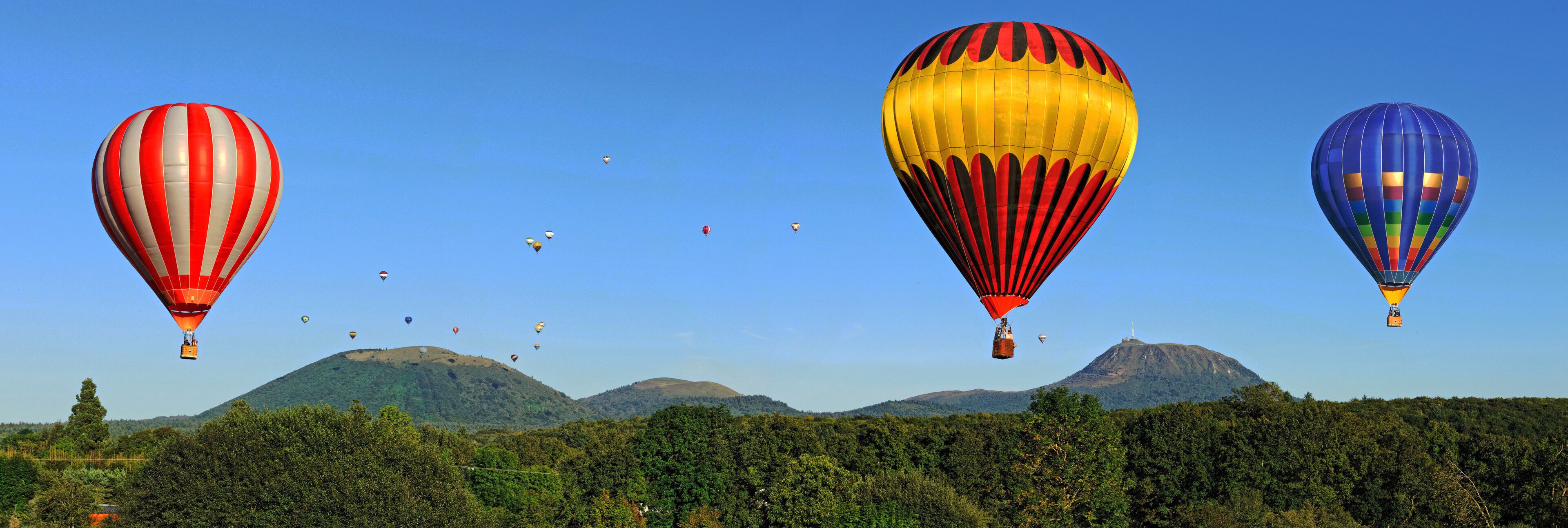 A landscape with a mountain range and hot air balloons in the sky.